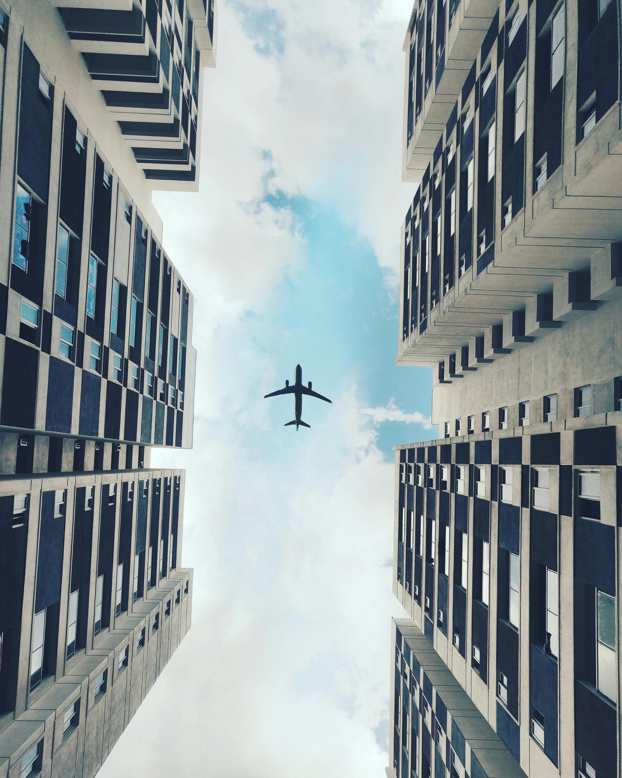 Low angle view of an airplane flying over modern skyscrapers against a bright sky in Chennai, India.